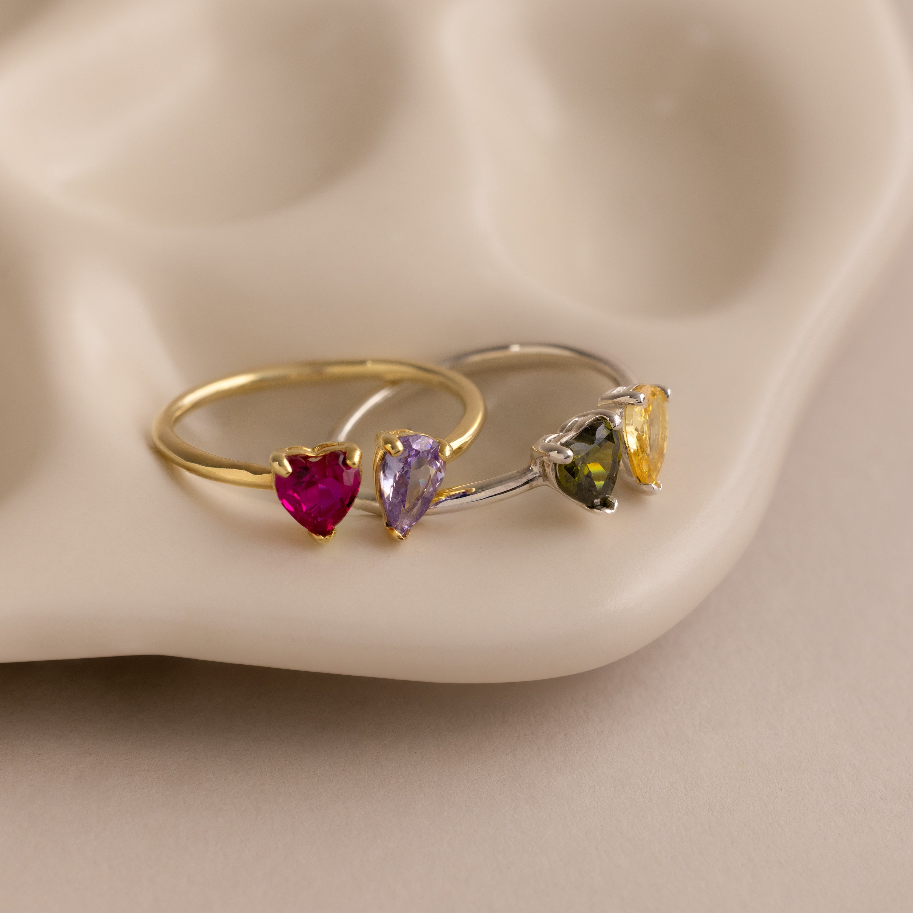 The Love Toi et Moi Ring features heart-shaped gemstones on gold and silver bands, perfect for stacking and displayed on a stylish beige ceramic dish.