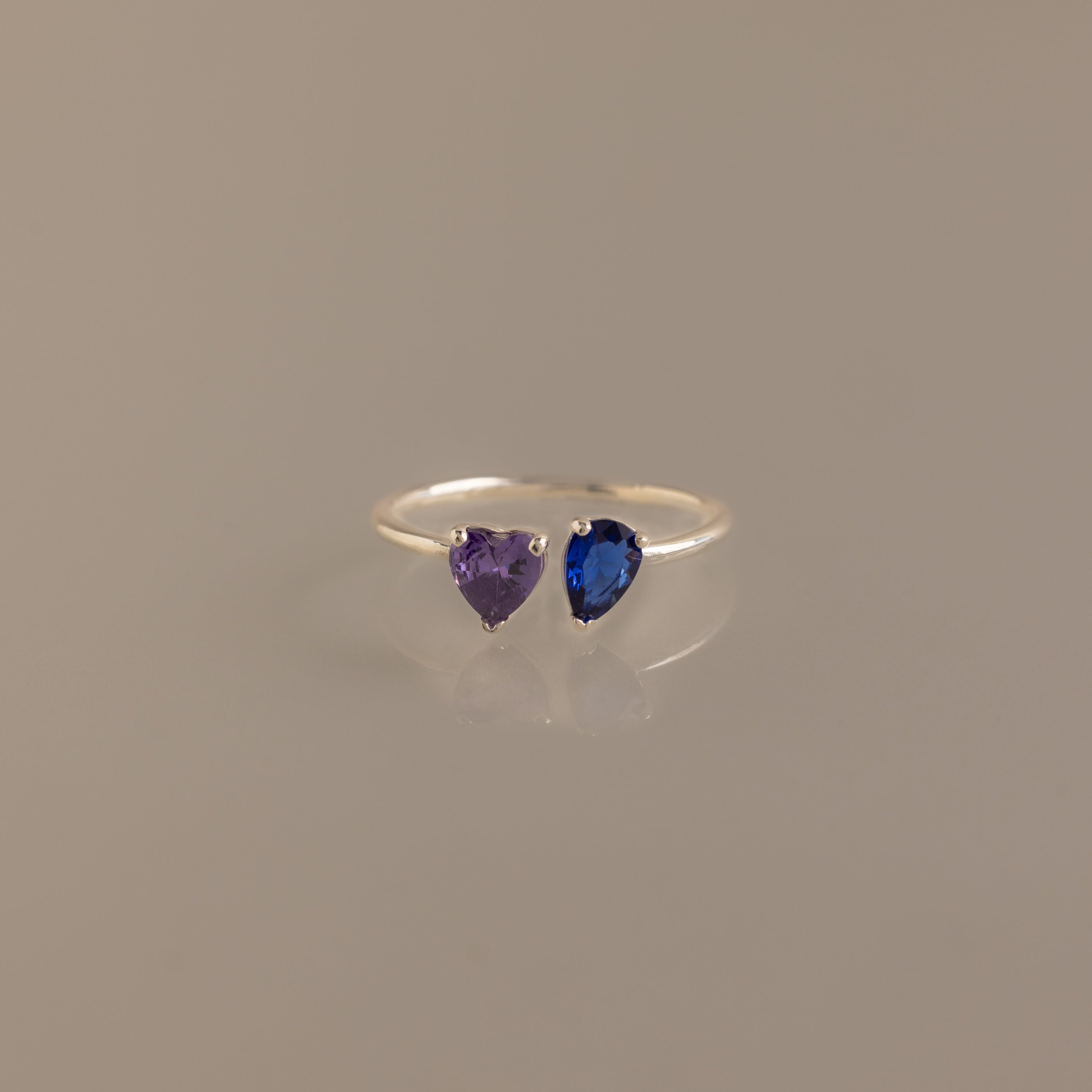 The Love Toi et Moi Ring in Silver features two heart-shaped gemstones—one purple and one blue—set side by side and shown against a plain neutral background.