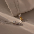 The Duo Birthstone Name Necklace in Sterling Silver features two silver necklaces—one with a yellow gemstone, one engraved with "Daisy"—offering personalized jewelry that shines beautifully on a neutral background.