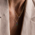 A person in a beige blazer wears layered gold necklaces, including the Duo Birthstone Name Necklace in Rose Gold featuring colorful rectangular stones and custom name engraving.