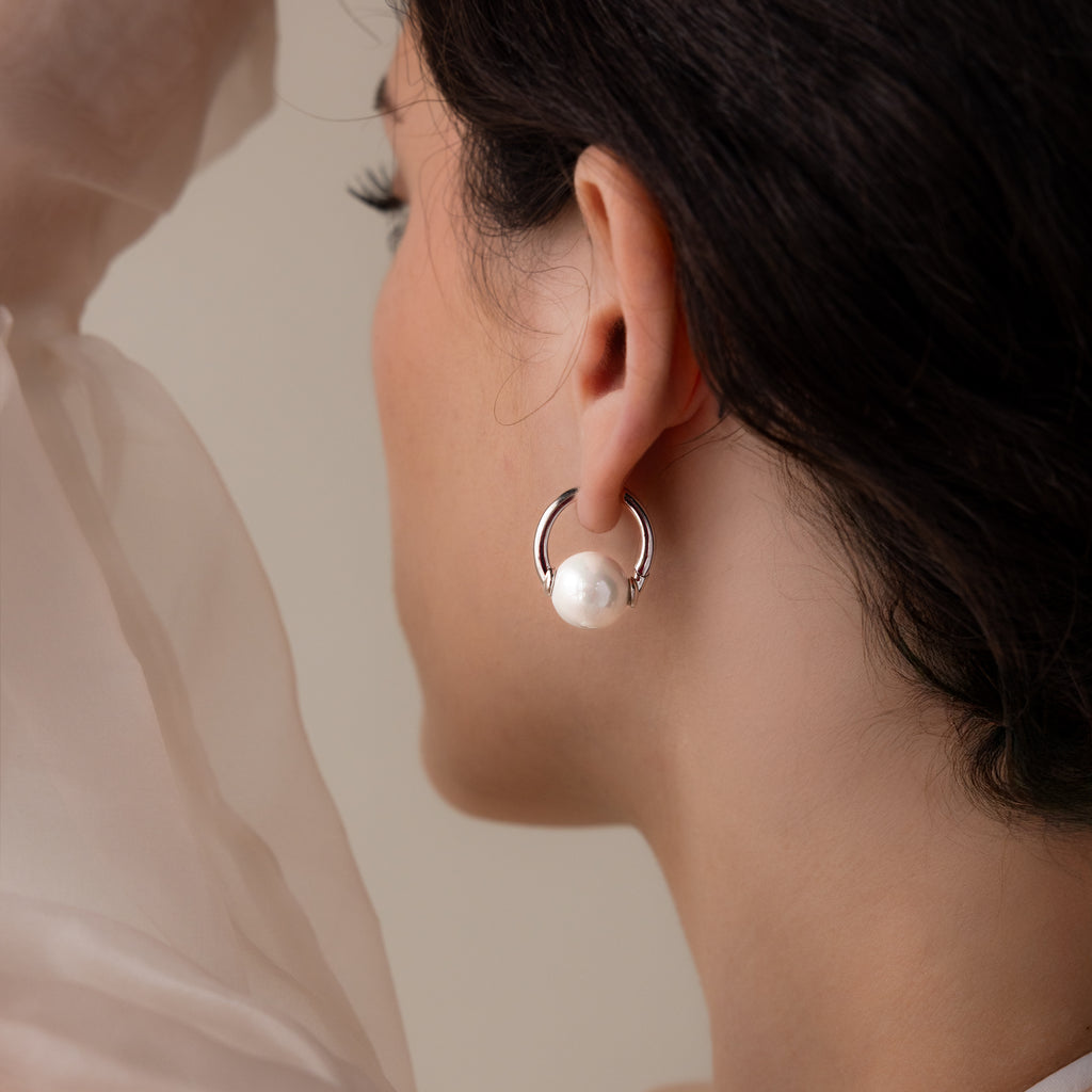 A woman shown from behind wears Bold Round Pearl Hoops in Silver, featuring large white pearls—a striking piece of modern jewelry.