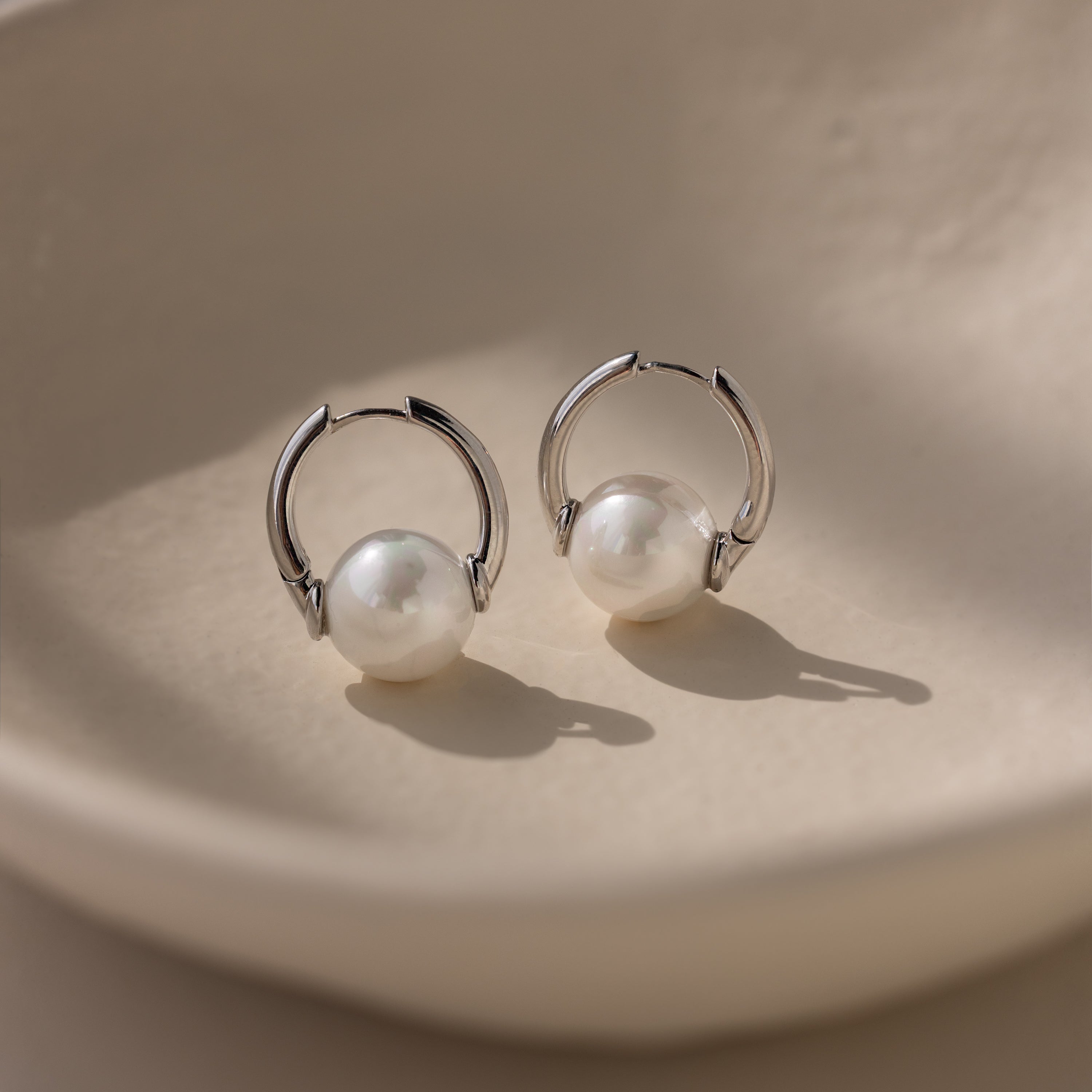 Bold Round Pearl Hoops—silver hoops with white pearls—make the perfect statement earrings for any occasion. Displayed on a cream surface in soft lighting.