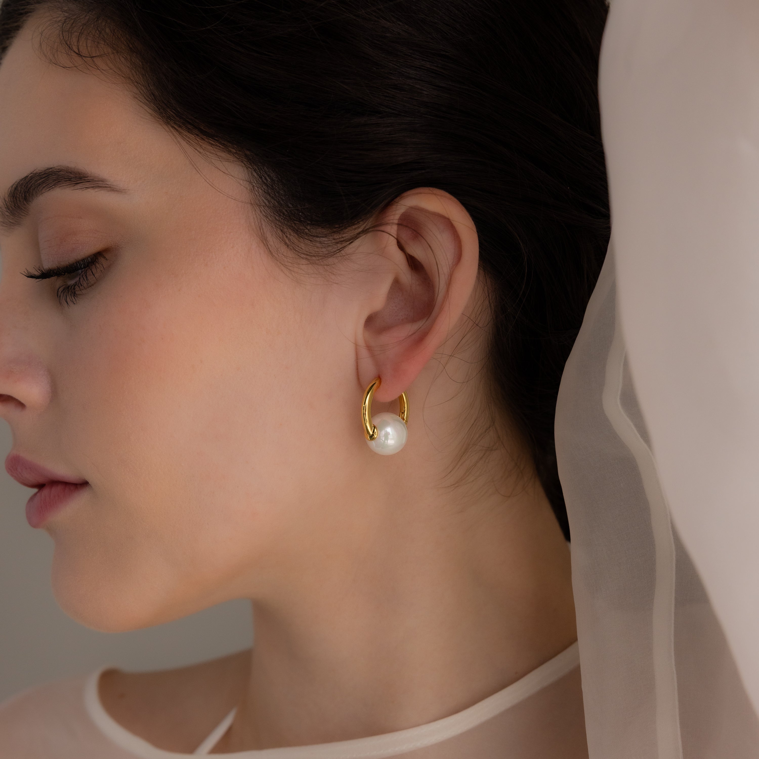 Woman with dark hair, eyes closed and draped in sheer white fabric, wears Bold Round Pearl Hoops—showcasing the stunning statement earrings.
