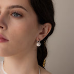 Close-up of a woman wearing Bold Round Pearl Hoops in Silver—modern silver hoop earrings featuring a white pearl, as she looks slightly to the left.