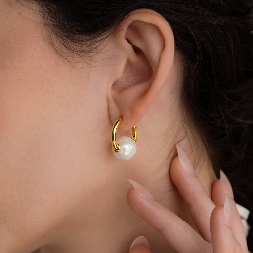 Close-up of a womans ear wearing the Bold Round Pearl Hoops, her hand near her face, highlighting these elegant statement earrings.