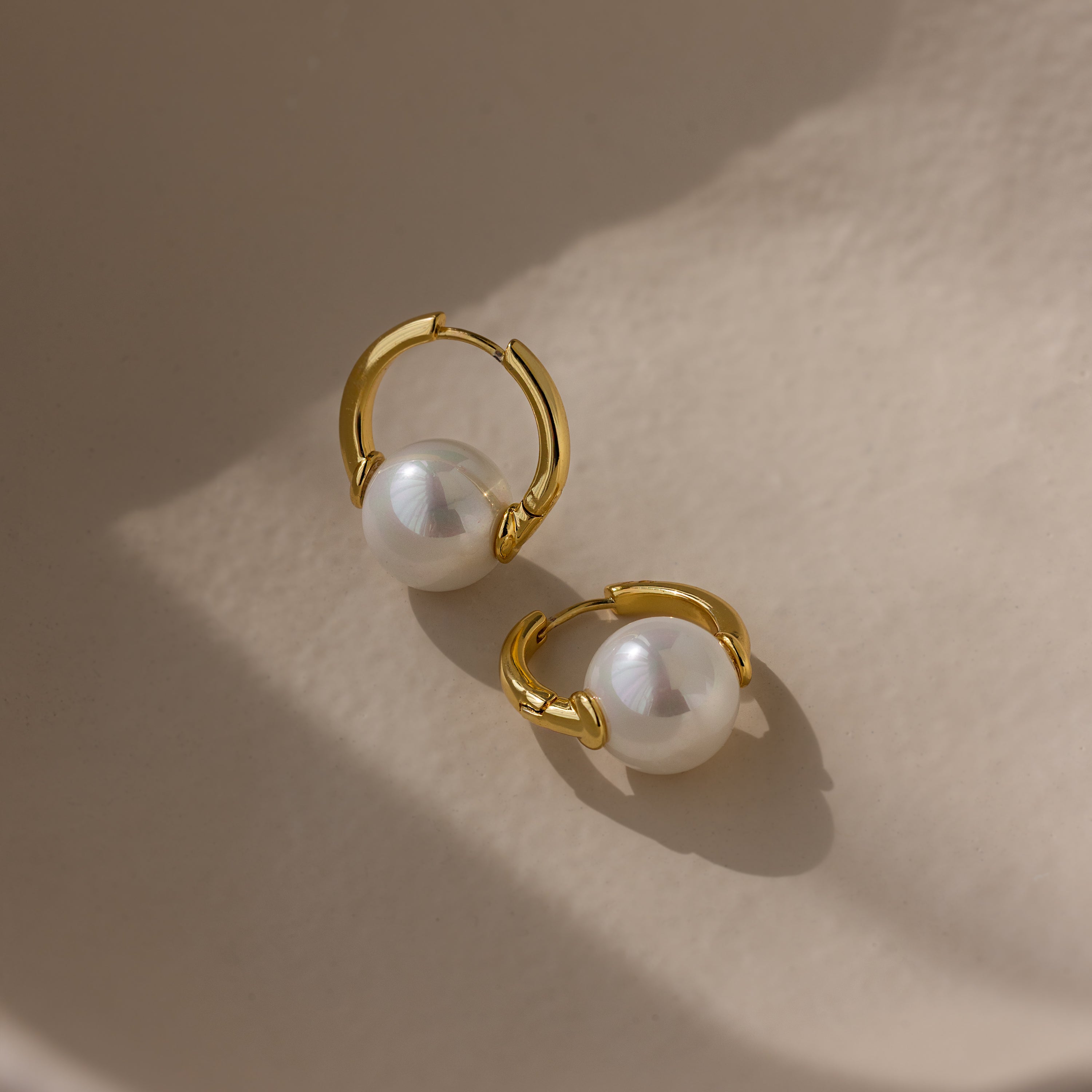 Bold Round Pearl Hoops featuring large white pearls shine on a smooth beige surface in soft light—ideal statement earrings to elevate any look effortlessly.