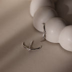 Silver ear jacket stud earrings with small diamonds on a beige surface