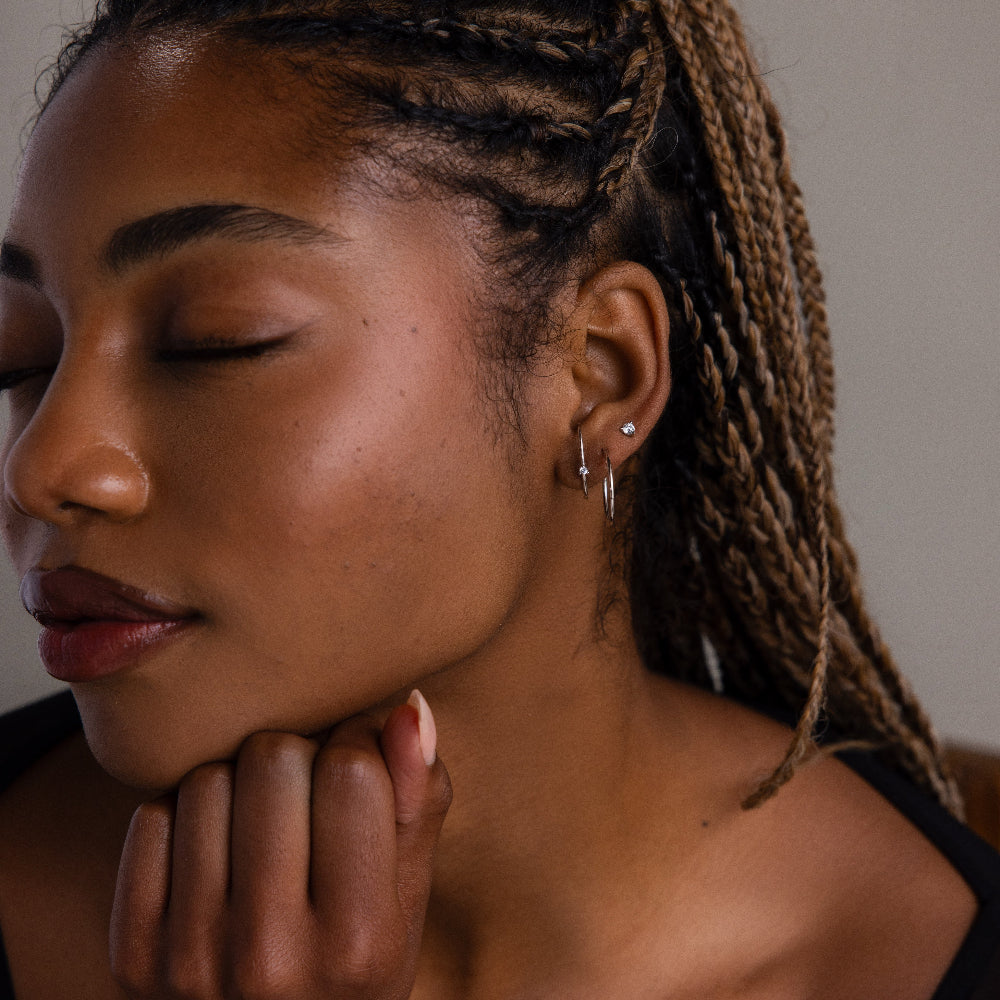 Close-up of a woman with a diamond studded ear jacket paired with a silver hoop and a simple diamond stud with braided hair and a neutral expression.