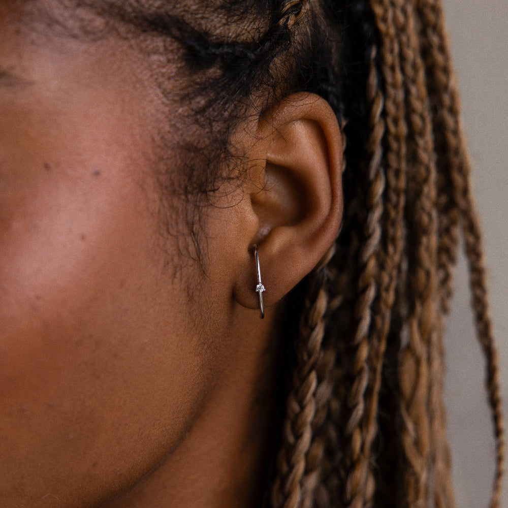 Close-up of an ear with a small ear jacket style diamond stud earring, hair styled in braids.