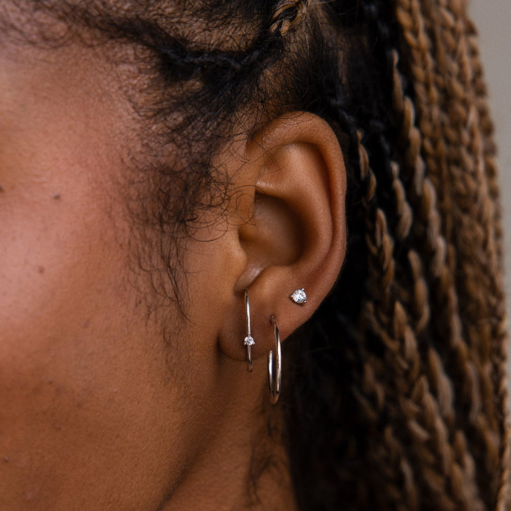 Close-up of an ear with silver earrings against a neutral background