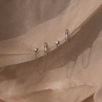 Two silver stud earrings with small stones and pave diamond ear cuffs on a beige fabric background