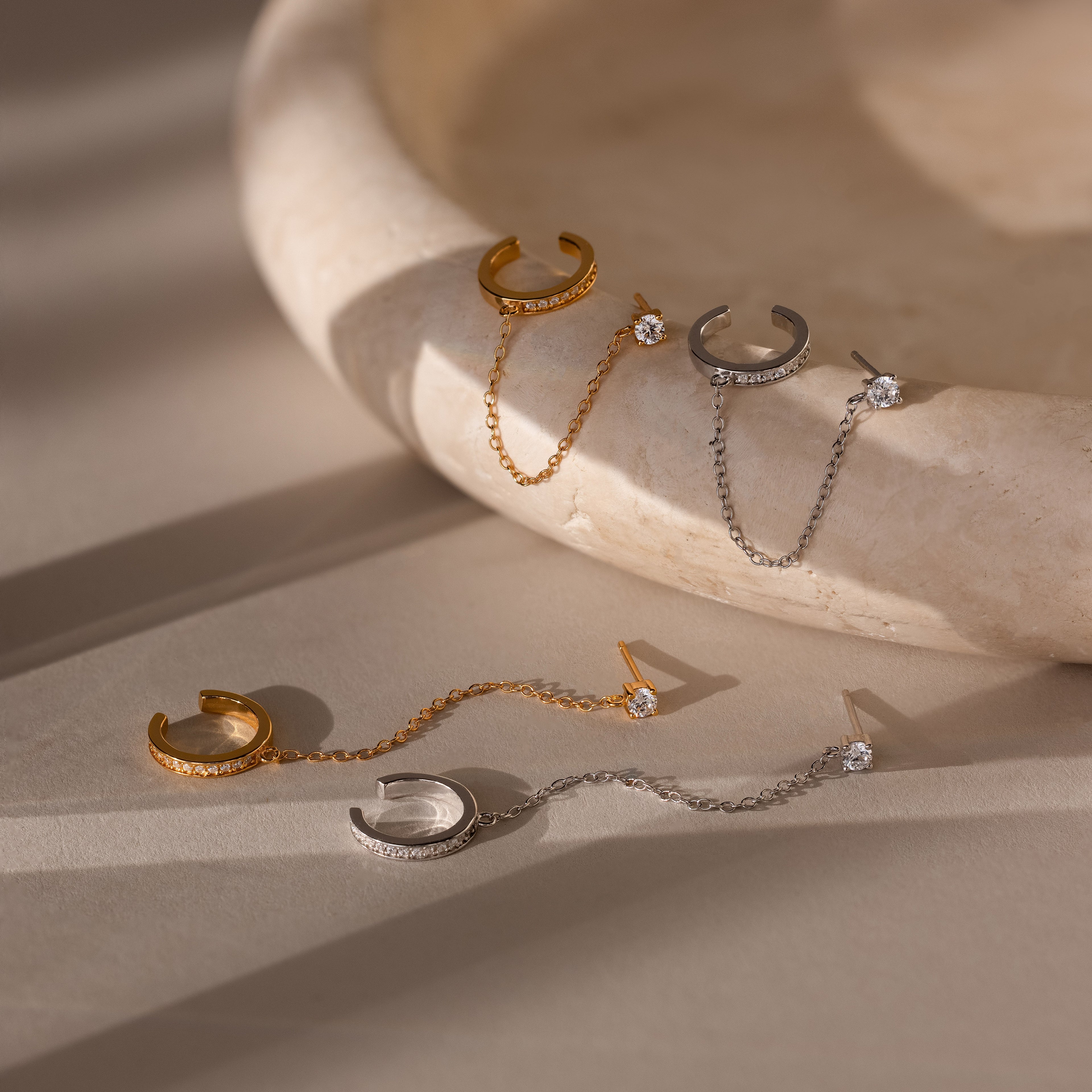 Set of gold and silver stud earrings each attached to an ear cuff on a beige stone surface
