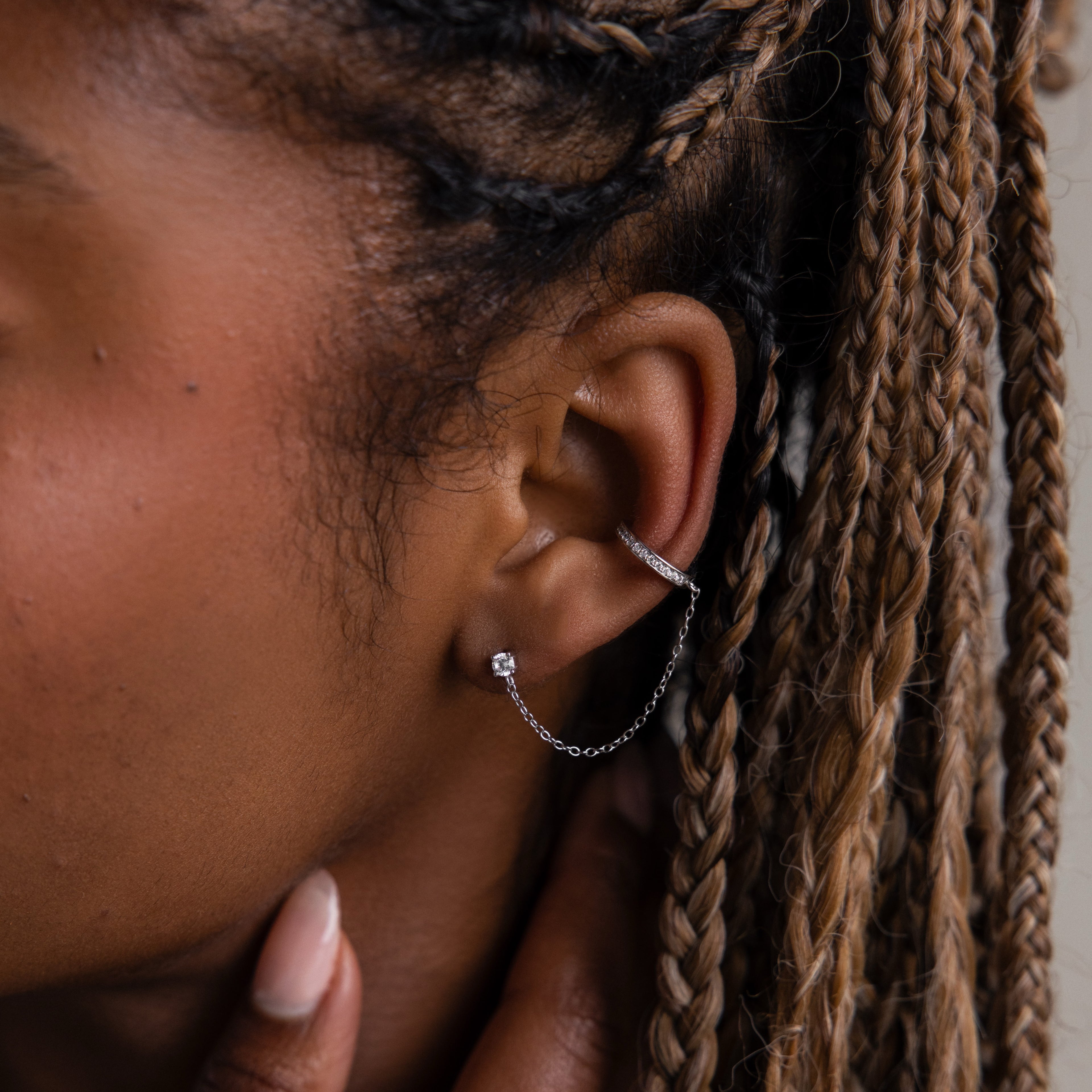 Close-up of an ear with a silver cuff earring attached to a diamond stud and braided hair.