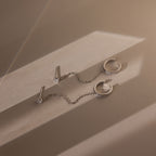Silver diamond stud earrings with pave ear cuffs attached by a chain on a beige surface