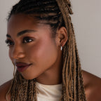 Woman with braided hair wearing a silver diamond hoop earring and a white top against a neutral background