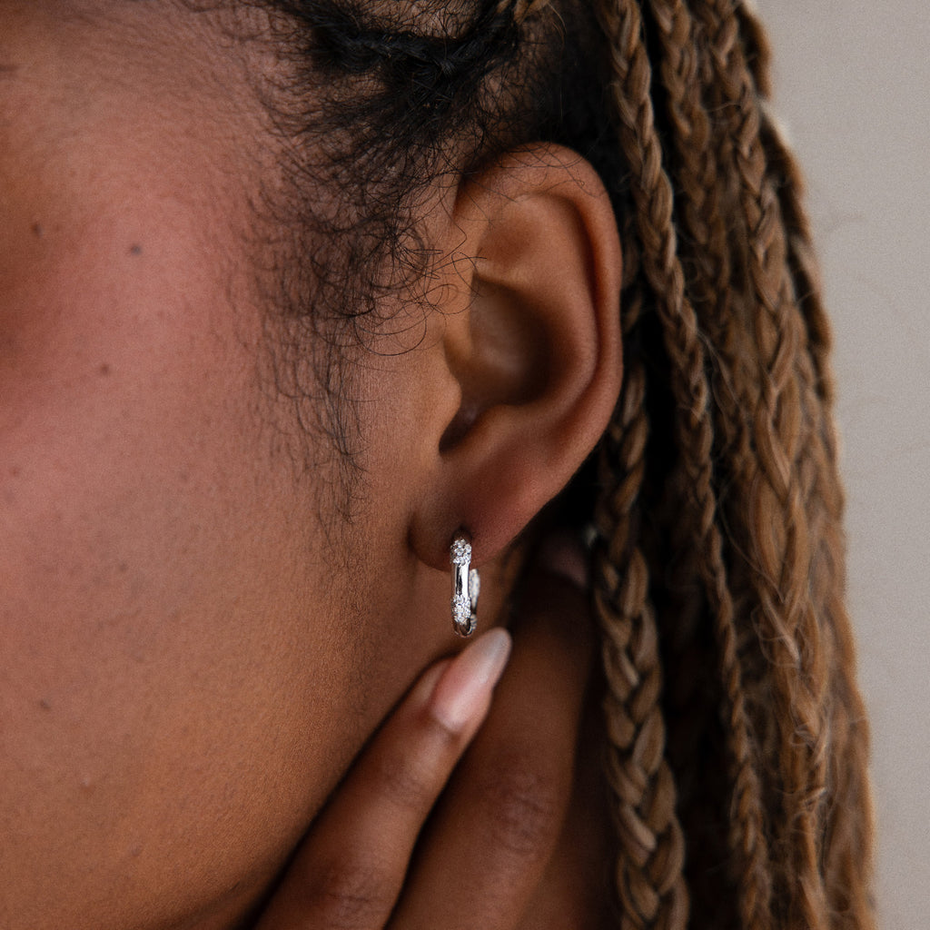 Close-up of an ear with a diamond hoop earring, hand adjusting hair.