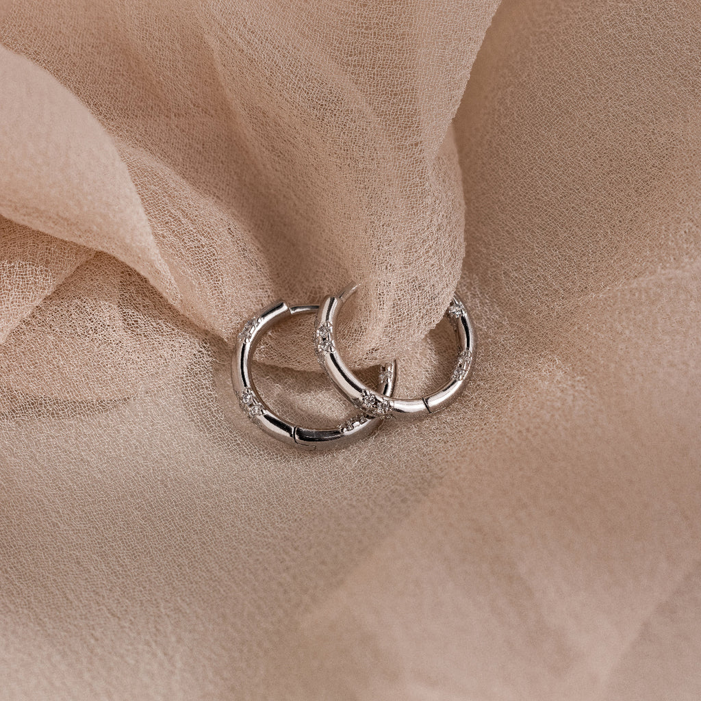 Pair of silver hoop earrings with diamonds embedded around the hoop on a soft beige fabric background