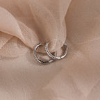 Pair of silver hoop earrings with diamonds embedded around the hoop on a soft beige fabric background