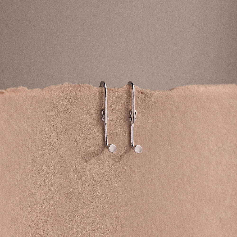 Two silver earring jackets on a beige background