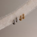 Two pairs of diamond hoop earrings in gold and silver on a textured fabric background.