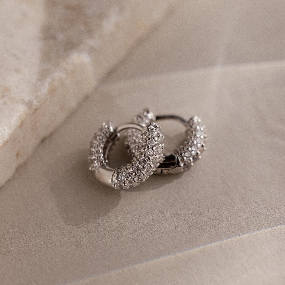 Pair of silver hoop earrings with clear gemstones on a beige surface
