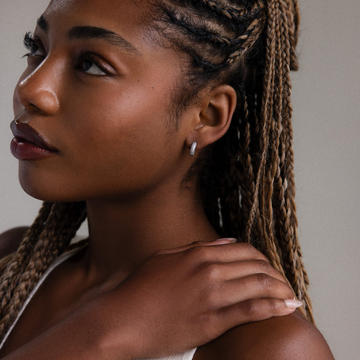 Woman with braided hair wearing silver diamond hoop earrings and a white top against a neutral background