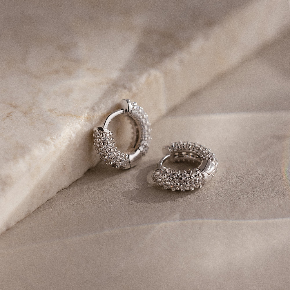 Silver hoop earrings with embedded stones on a beige stone surface