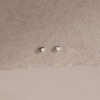 Tiny silver heart-shaped earrings on a beige background