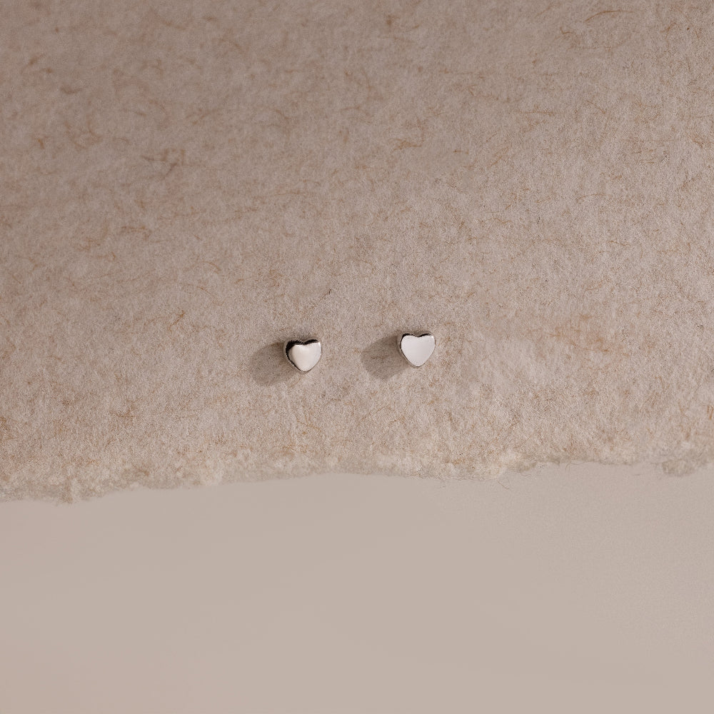 Tiny silver heart-shaped earrings on a beige background