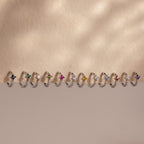 Twelve Athena Blue Zircon Huggies, silver rings with vivid blue gemstones, are displayed in a row on a beige background.