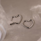 Heart-shaped silver hoop earrings on a beige surface