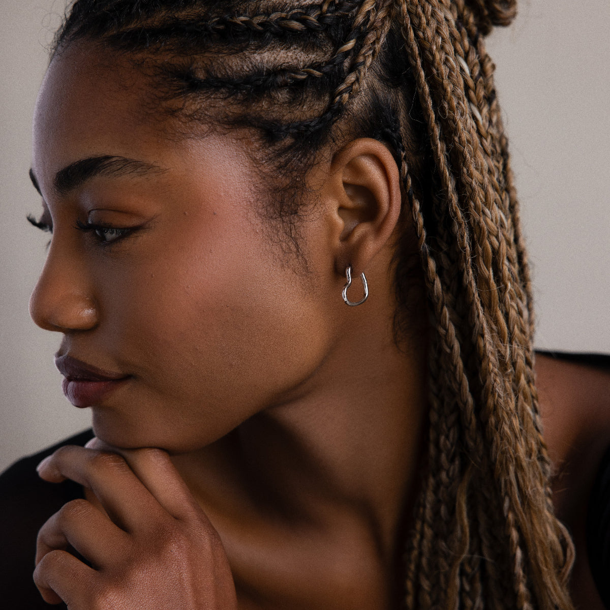 Close-up of a woman with braided hair wearing a small silver heart hoop earring.
