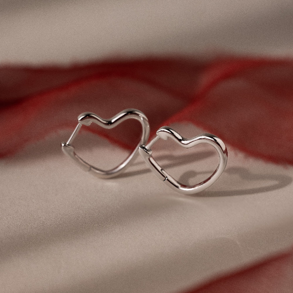 Silver heart-shaped hoop earrings on a soft fabric background