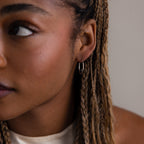 Close-up of a person with braided hair wearing a silver hoop earring.