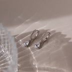 Pair of silver teardrop diamond earrings on a textured surface with soft lighting
