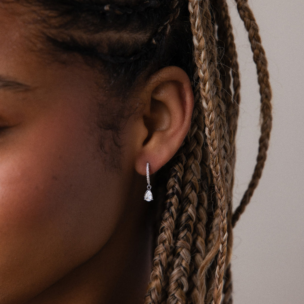 Close-up of an ear with a silver diamond huggie hoop earring against a neutral background