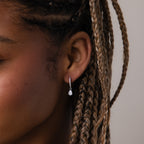 Close-up of an ear with a silver diamond huggie hoop earring against a neutral background