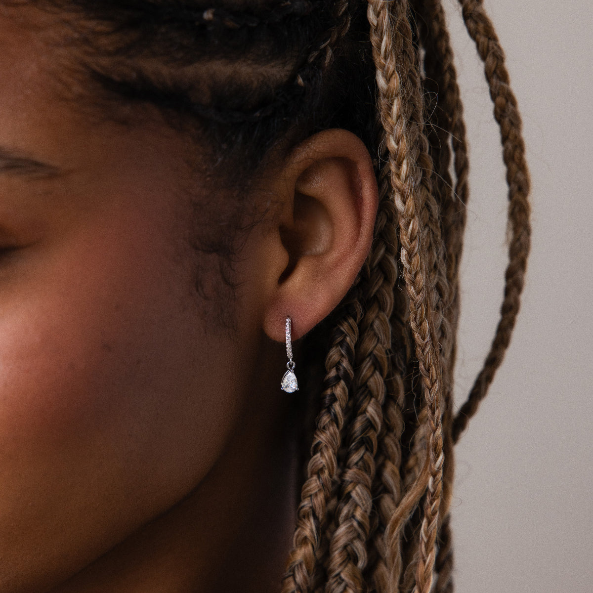 Close-up of an ear with a silver diamond huggie hoop earring against a neutral background