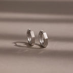 Pair of silver huggie hoop earrings on a beige background