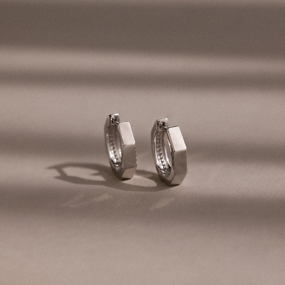 Pair of silver huggie hoop earrings on a beige background