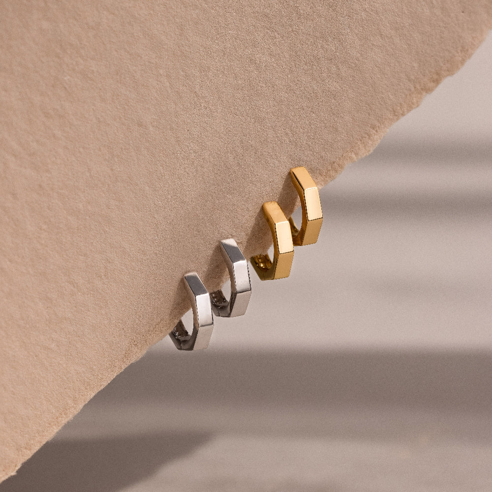 Two gold and silver hoop earrings on a beige background