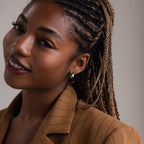 Woman with braided hair wearing silver hoop earrings and a brown pinstripe blazer against a neutral background