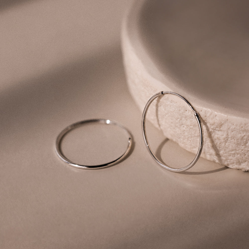Two silver hoop earrings on a beige surface with a textured bowl in the background.