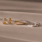 Gold and silver Art Deco Diamond Earrings & Ring Set with rectangular gemstones evoke vintage glamour, elegantly arranged on a soft beige surface with gentle shadows.