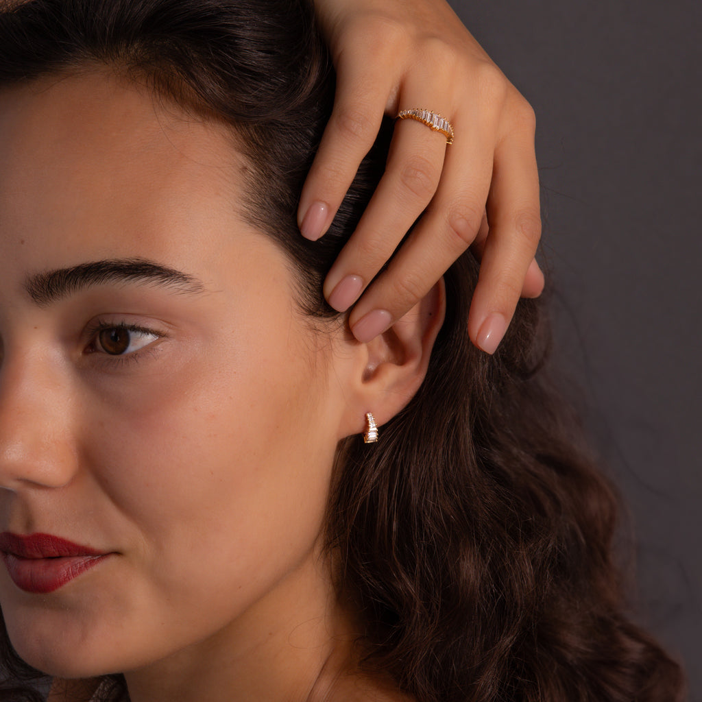 A woman with wavy hair exudes vintage glamour, wearing the Art Deco Diamond Earrings & Ring Set in gold, posing elegantly with her hand near her face.