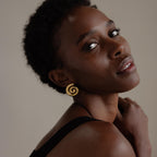Woman with short curly hair wearing a black top and Bold Spiral Stud Earrings, looking over her shoulder.