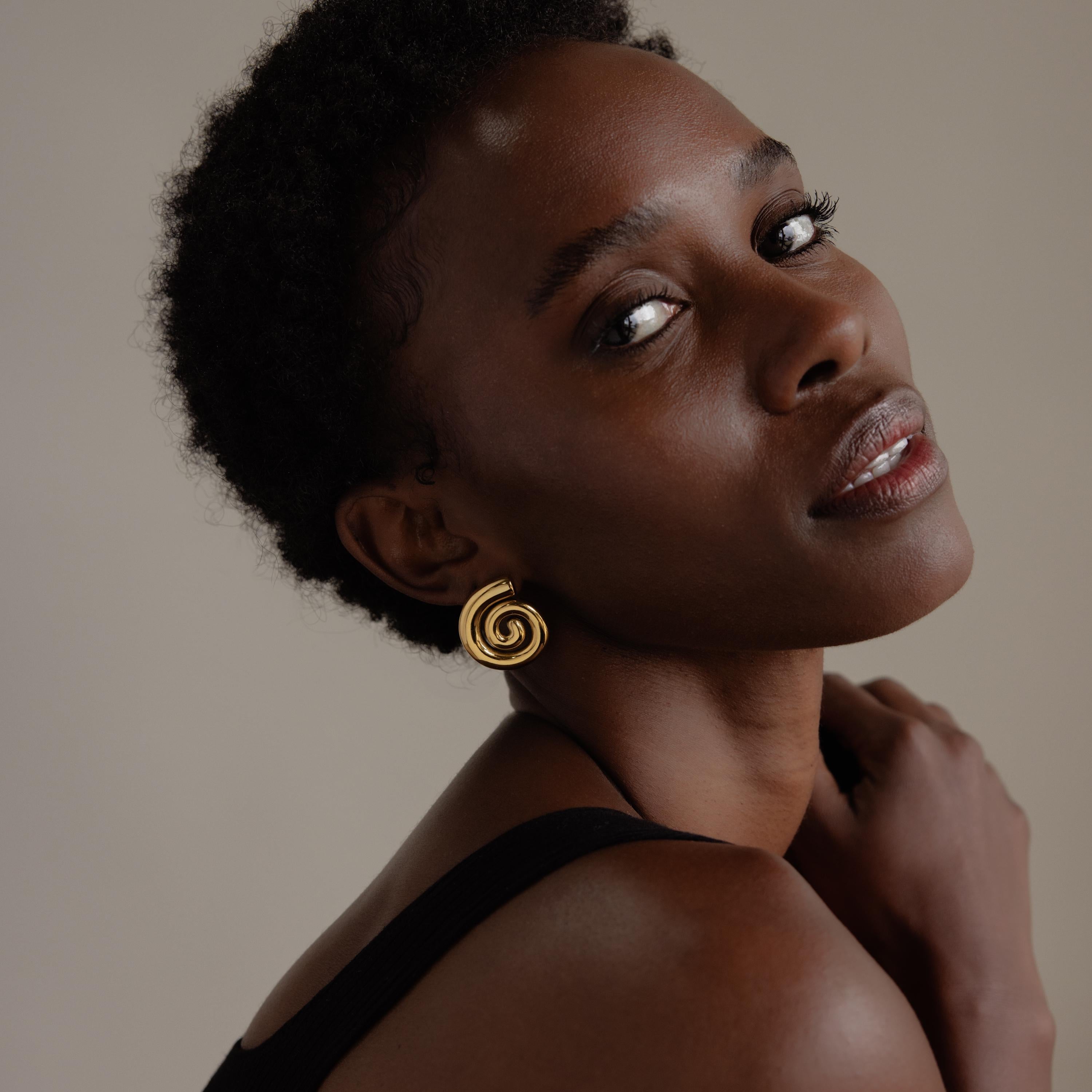 Woman with short curly hair wearing a black top and Bold Spiral Stud Earrings, looking over her shoulder.