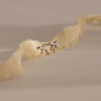 A pair of silver bow stud earrings placed on an ivory frayed-edge fabric.