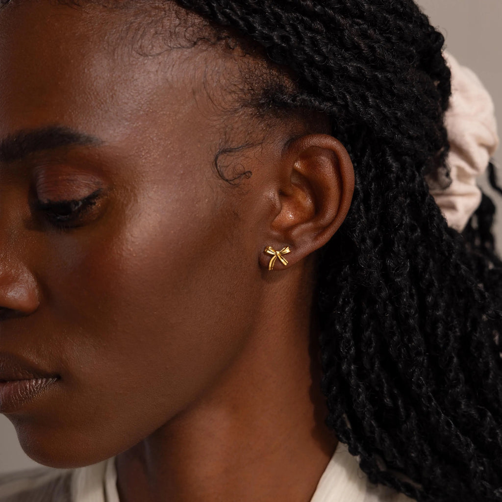 A wider side profile view of the woman wearing gold bow studs.