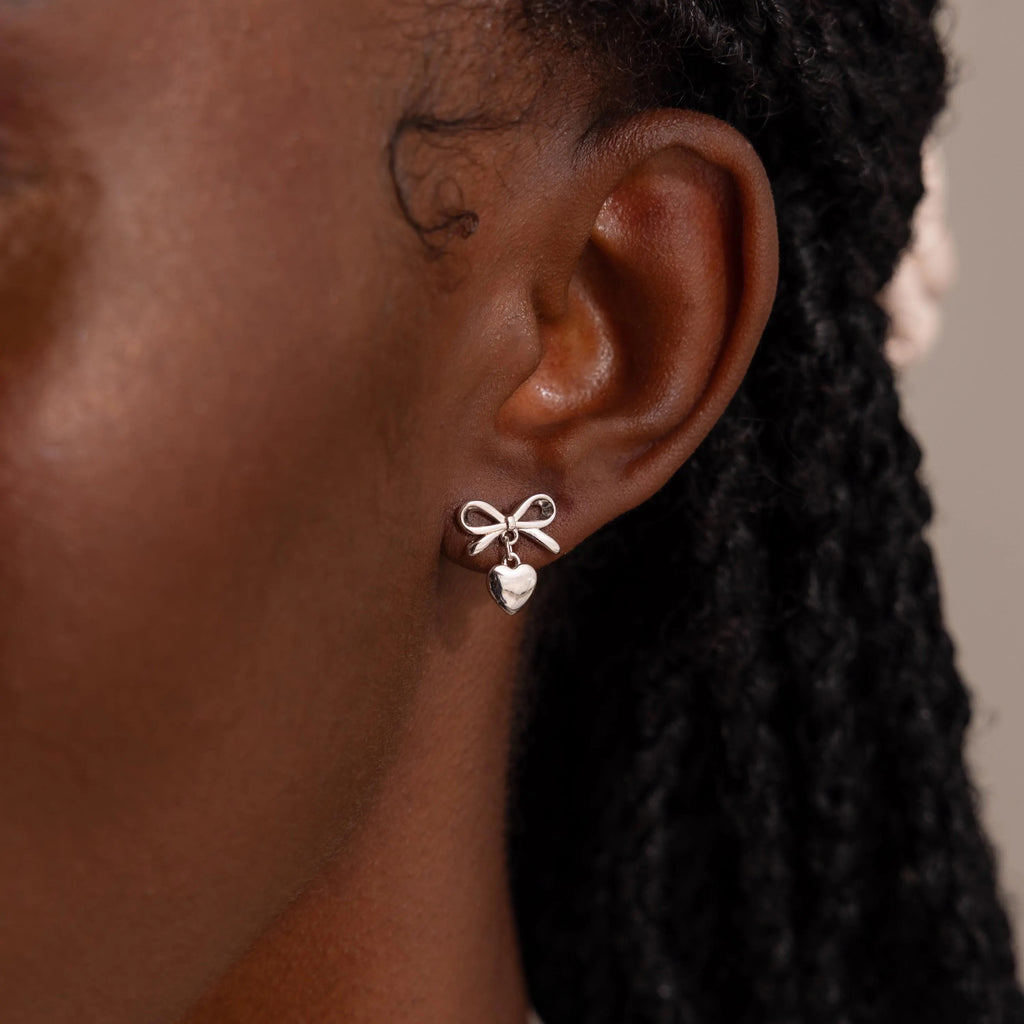 Close-up of a woman wearing a silver version of the bow heart stud earring, which sits elegantly against her earlobe.